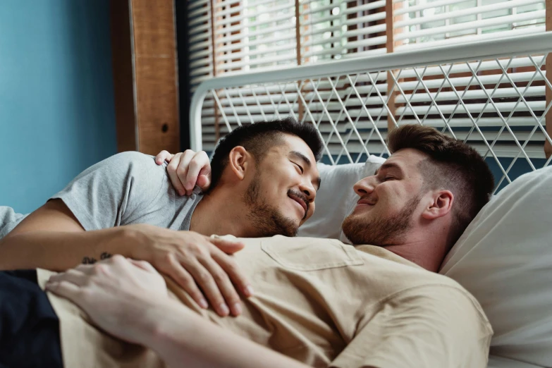 two men lying in bed, the male laughing