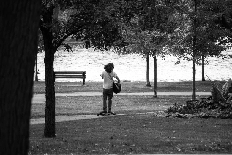 a boy is looking at the water as he stands on a skateboard