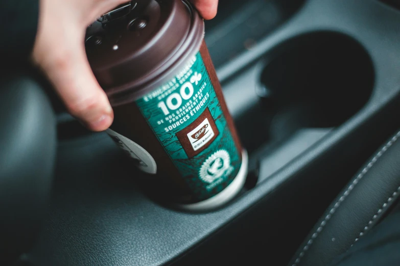 a person opening a bottle into a car cup holder