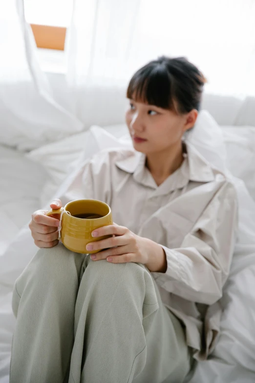 a woman sitting on top of a bed holding a cup