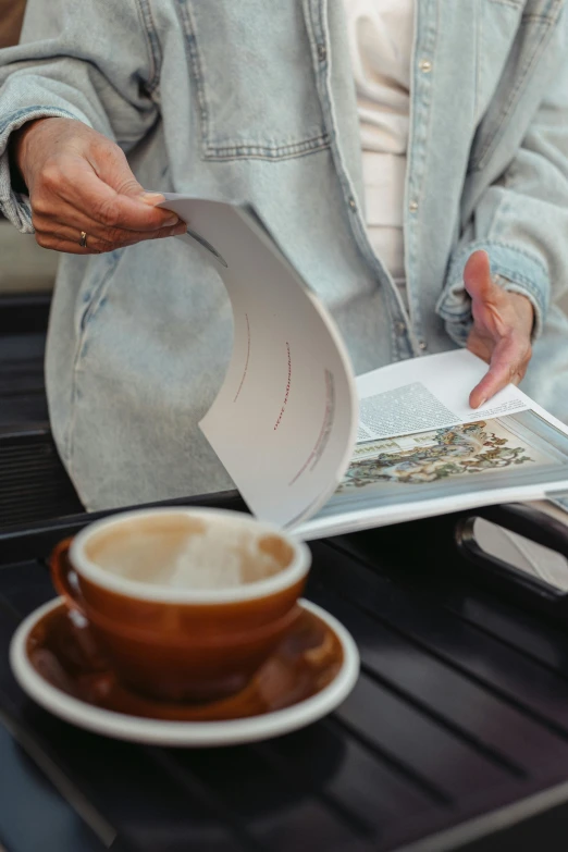 a woman is sitting in front of a coffee cup reading the cookbook