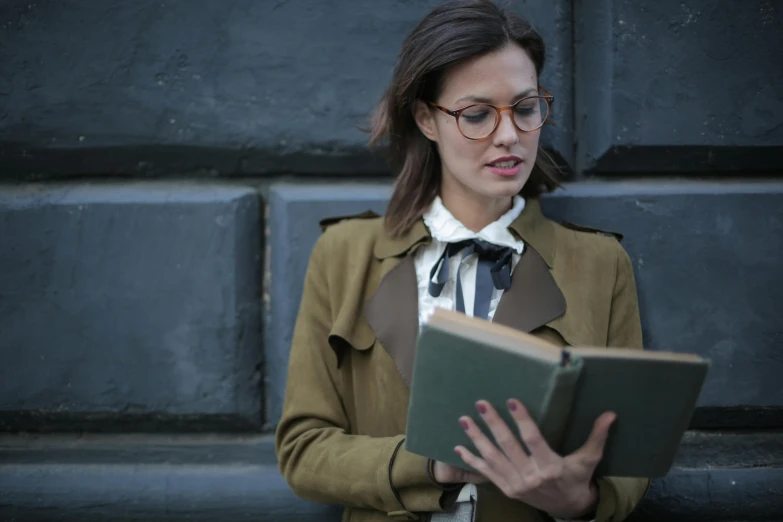 a woman wearing glasses and a coat reading a book