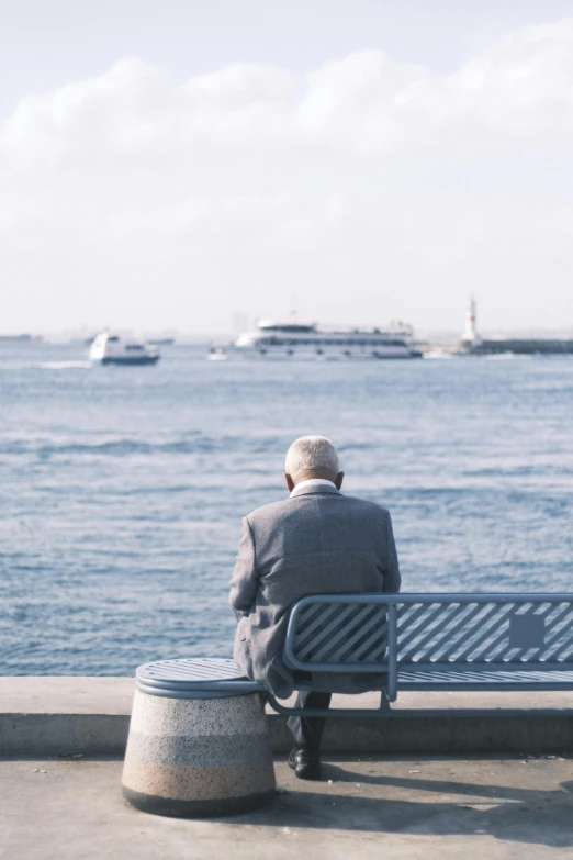 the man is sitting on the bench looking out at the water