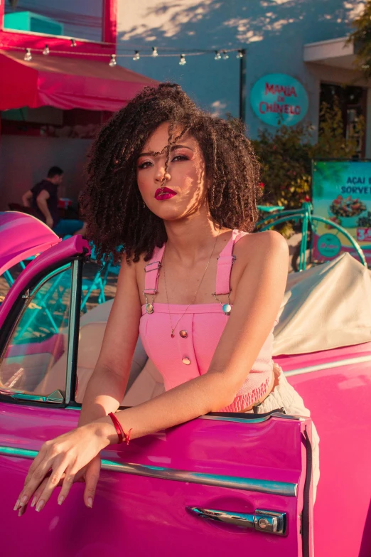 woman posing with hands on the back of a pink car