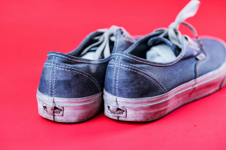 blue slip on sneakers are lying against a bright red background