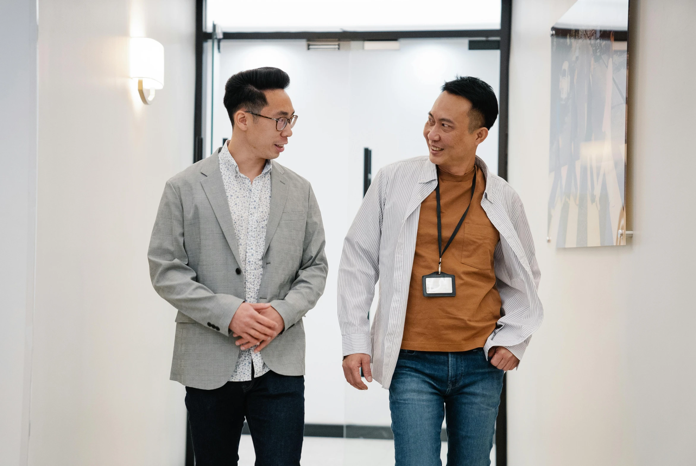 two asian men are standing in a hallway talking