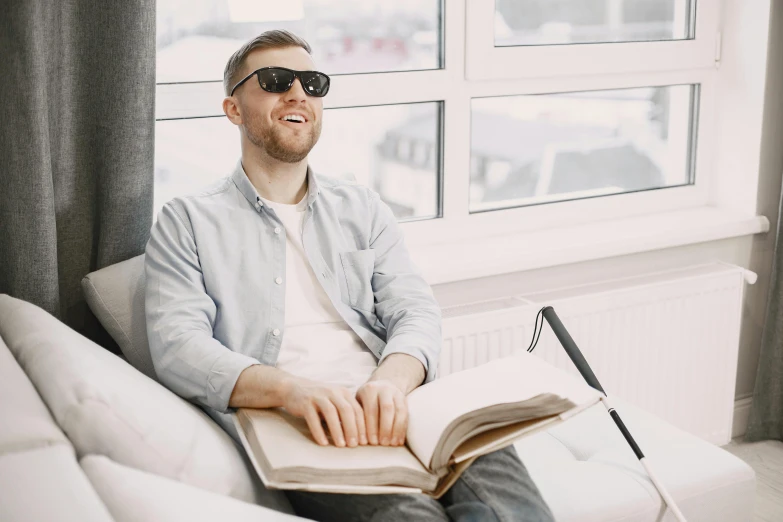 man in glasses sits on a couch and holds open book