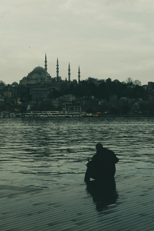 a person kneeling in the water watching some buildings on land