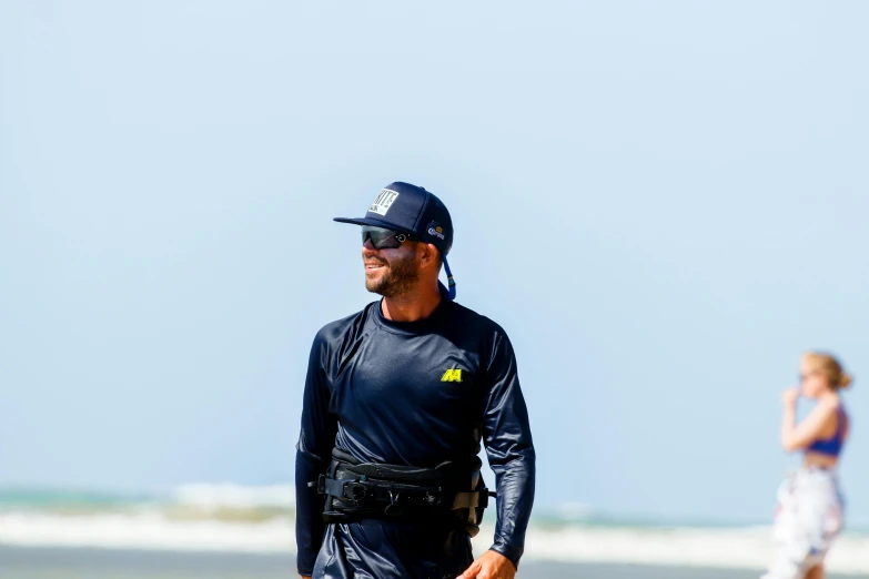 a man walking on the beach with a hat