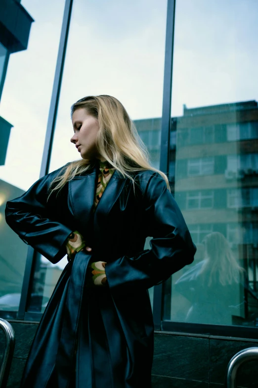 a woman in a trench coat and tie standing in front of a window