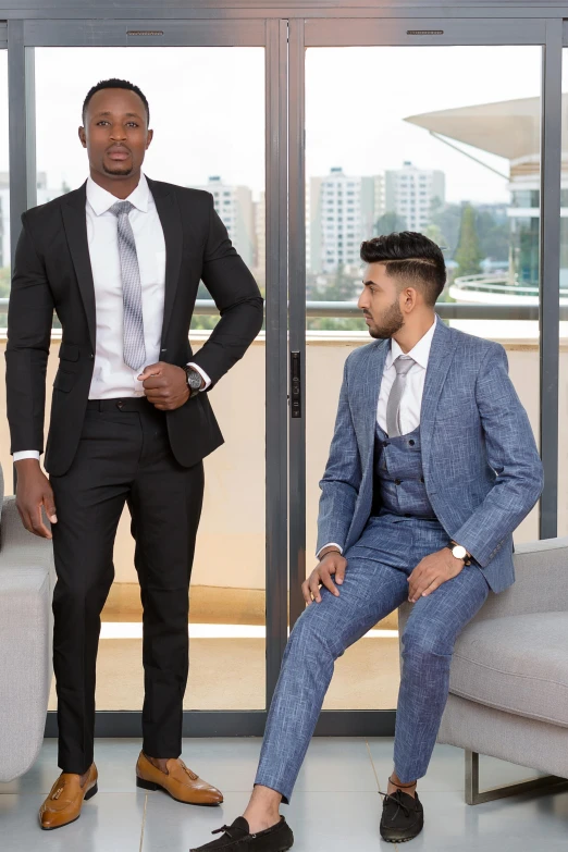 two men wearing suits, one sitting in a chair