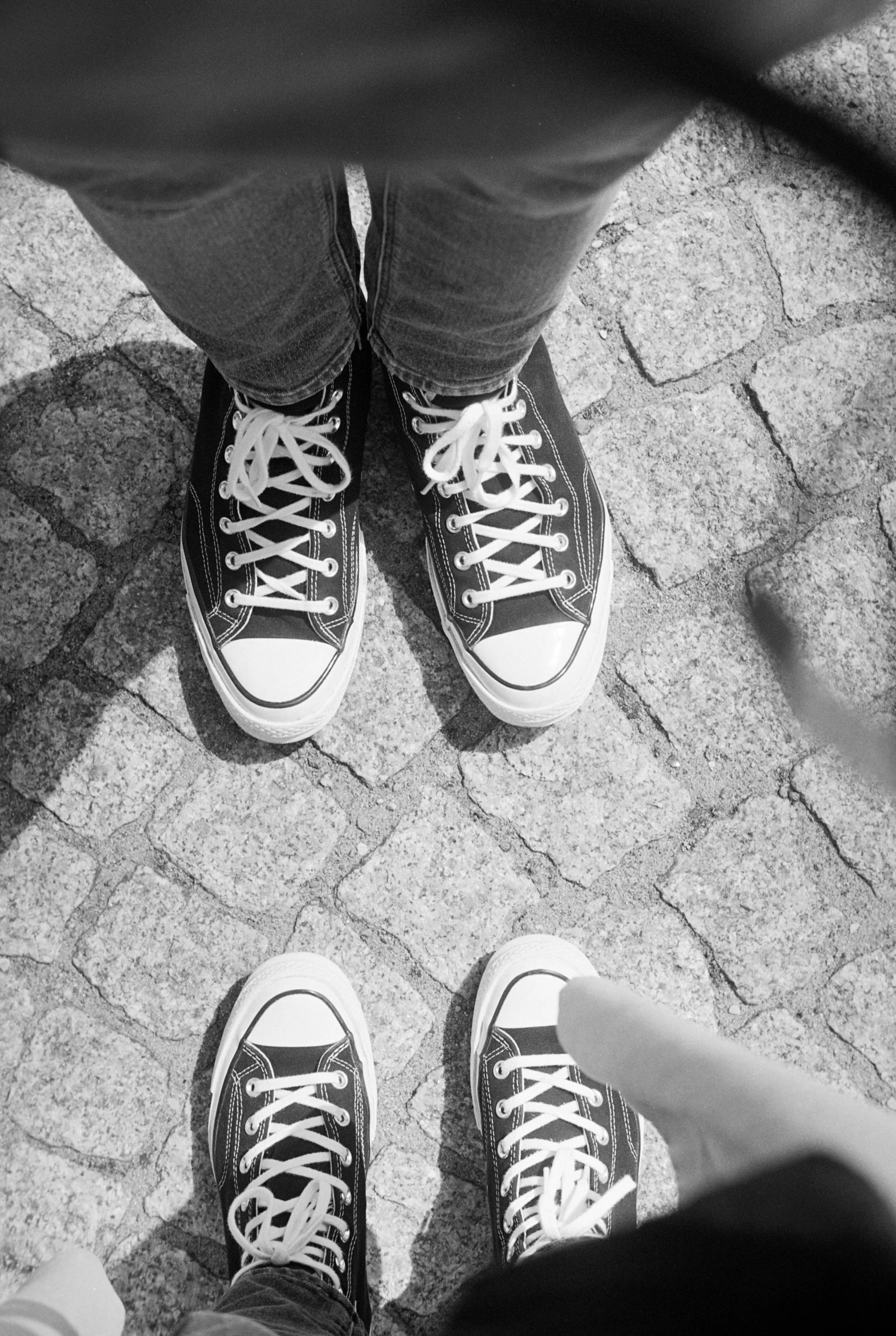 two feet standing on the cement pavement with white converse sneakers