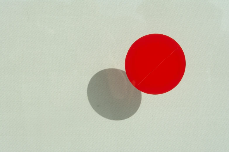 a light red ball casts a shadow against a white wall