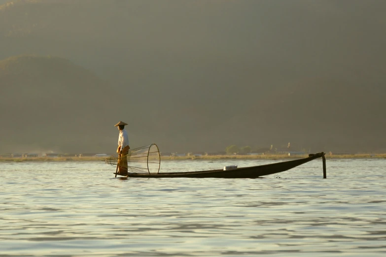 man standing in a boat on water with mountains in background