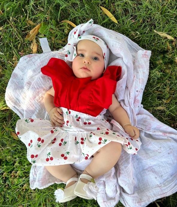 a baby in a dress lies on a blanket on the grass