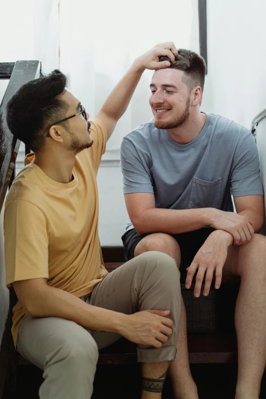 two men are sitting together and one is combing his hair