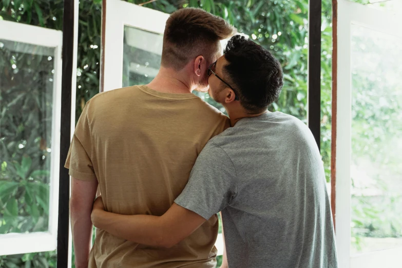 two young men hugging each other by a large window