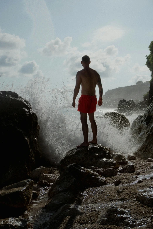 a man in red shorts standing on the rocks at the ocean
