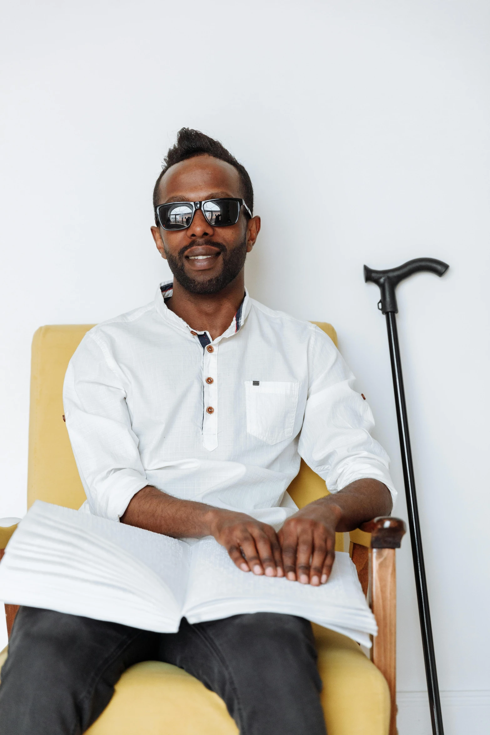 a black man wearing glasses and a white shirt sitting on a chair reading a book