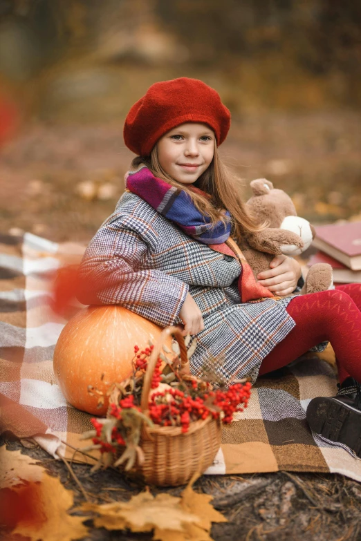 girl holding teddy bear on picnic blanket in autumn