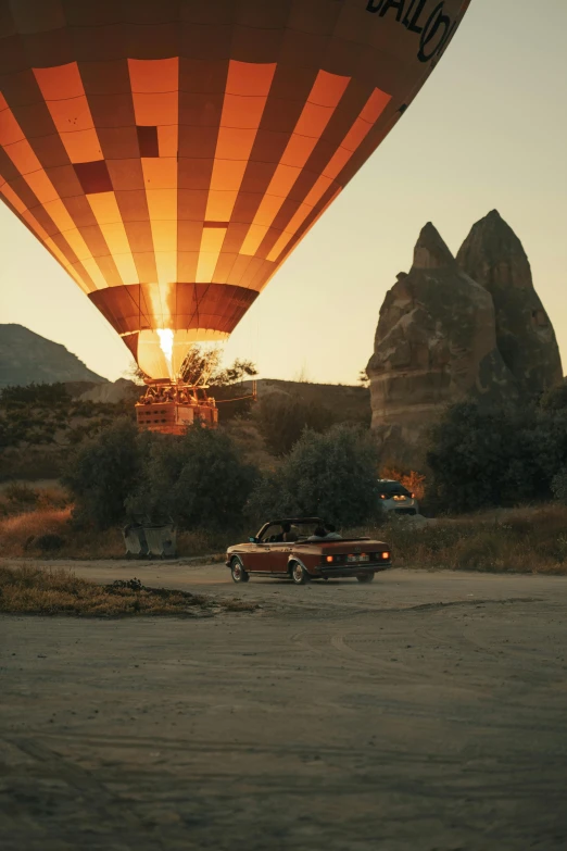 a car sits at the edge of the road beneath an up and away  air balloon