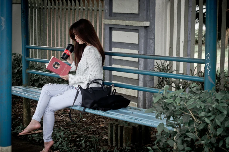 the woman sitting on the bench is holding her book