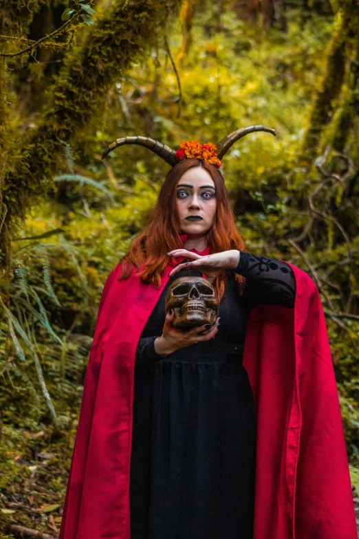 a woman in a red cape holds up a human skull