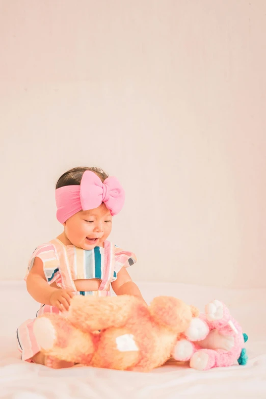 an infant girl is sitting on a bed with a pile of stuffed animals