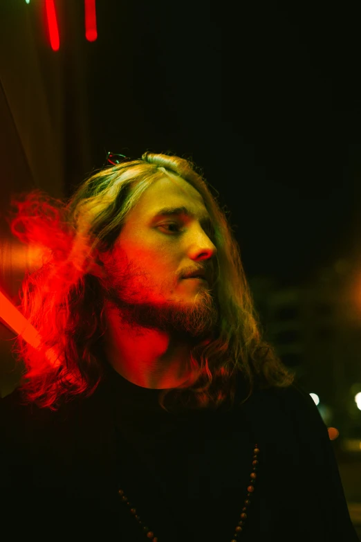 a bearded man with long hair stands in front of a neon colored background