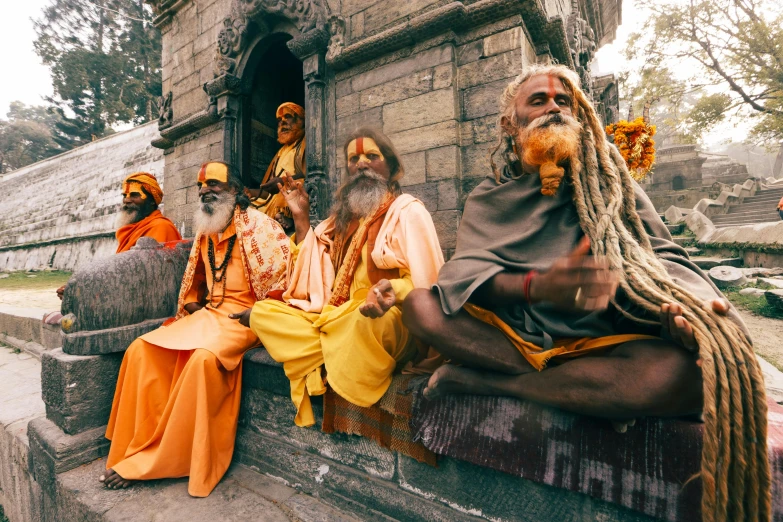 men wearing orange sit together in front of a temple