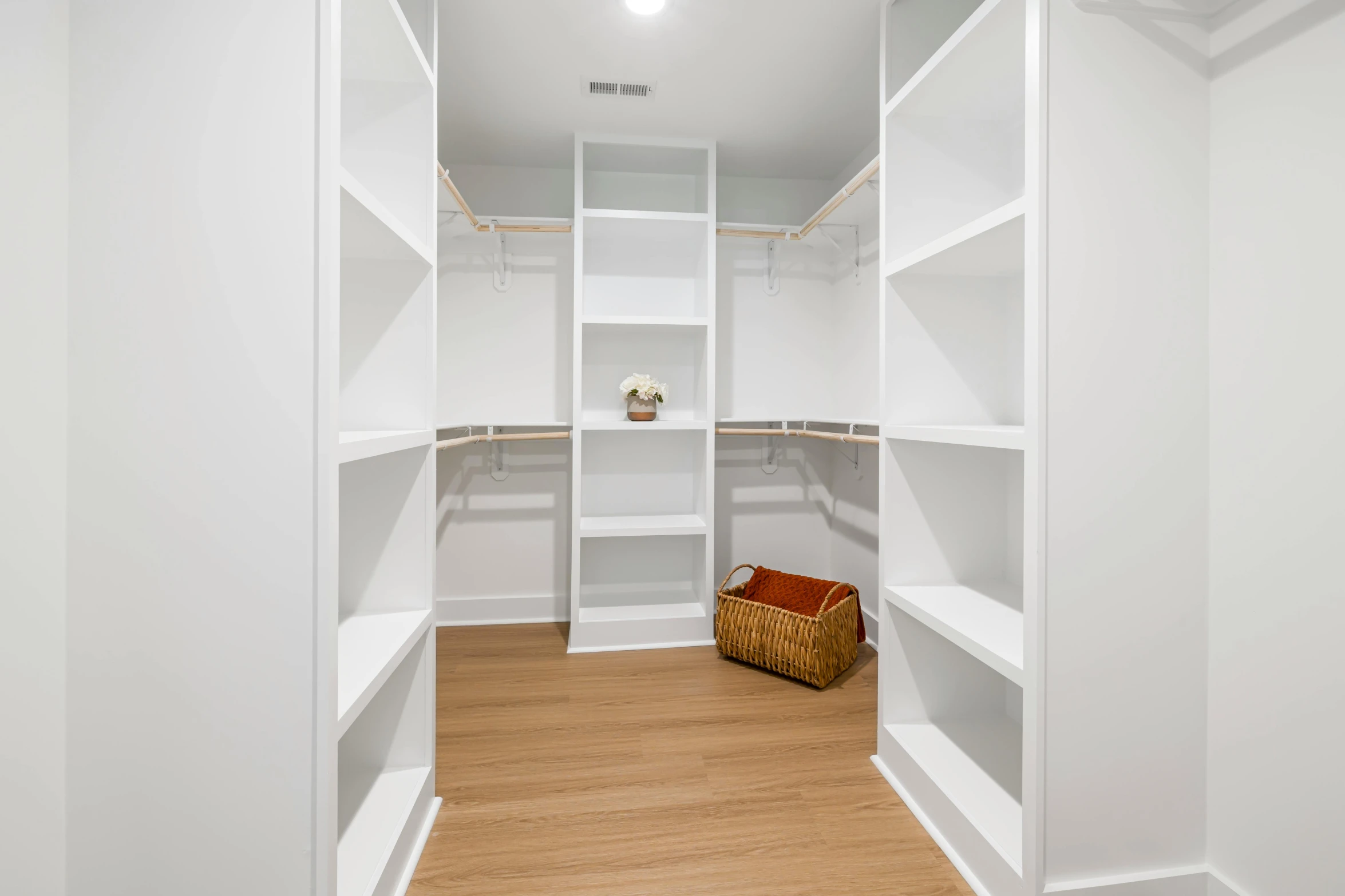 the empty white closet has wood flooring and shelves