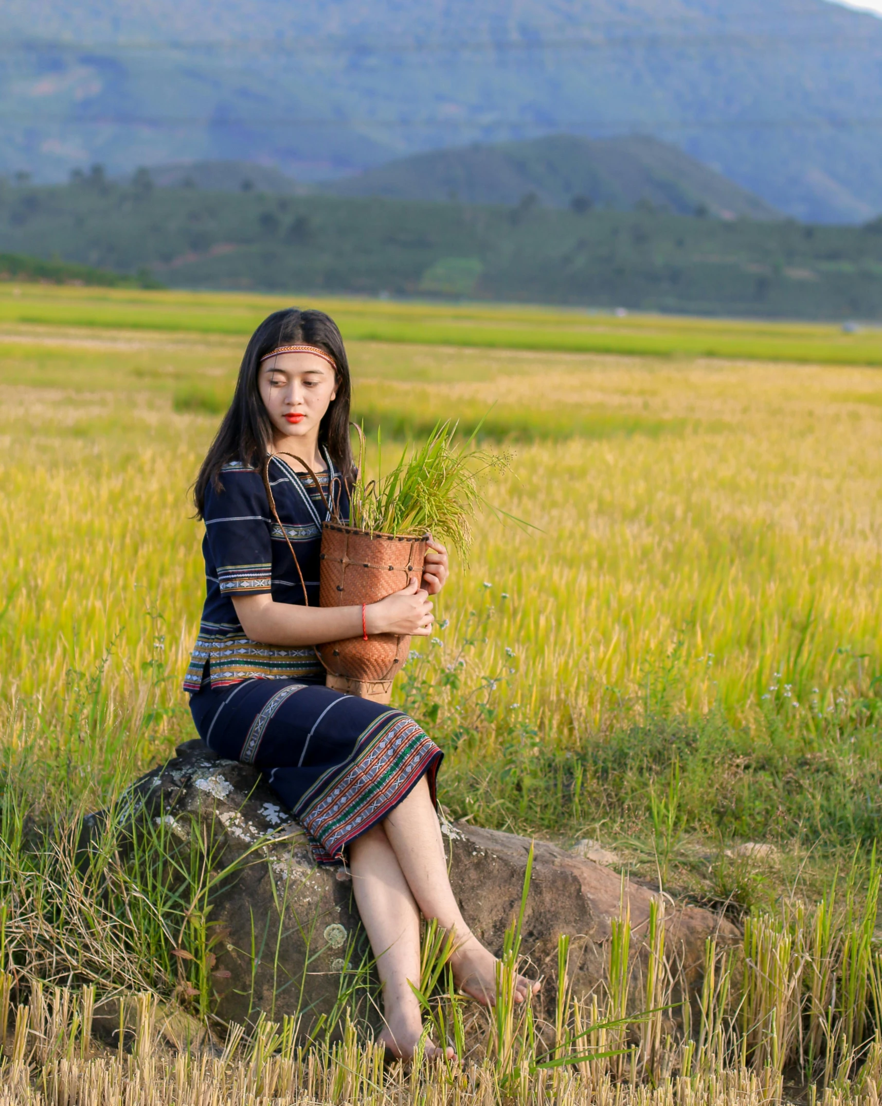 a woman sits on top of a rock and holds a potted plant