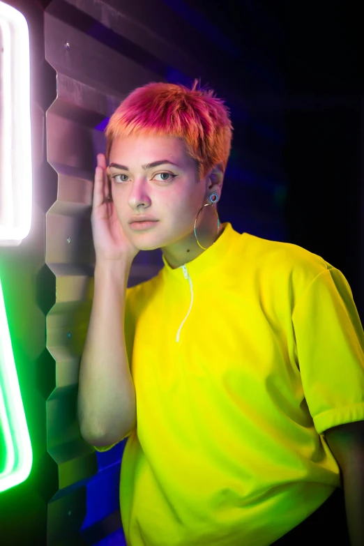 a young person with pink hair posing next to a neon sign