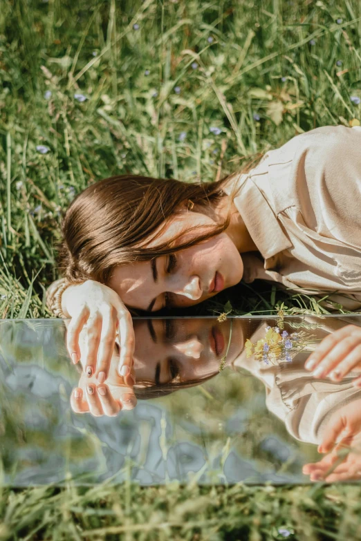 woman laying in the grass on her stomach touching water