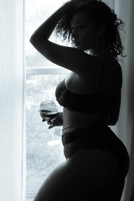 a black and white po of a woman in underwear looking into a window