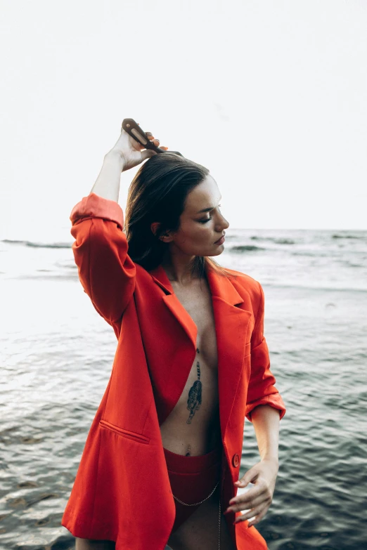 a beautiful woman in an orange jacket standing next to a body of water