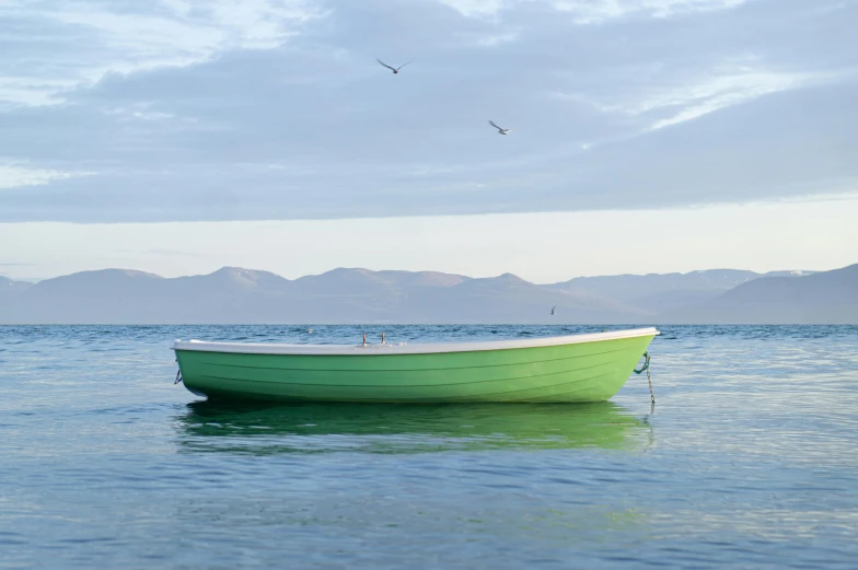 the small green boat is floating on clear water