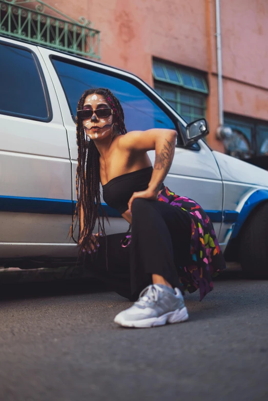 a woman sitting in front of a car with her arm on the tire