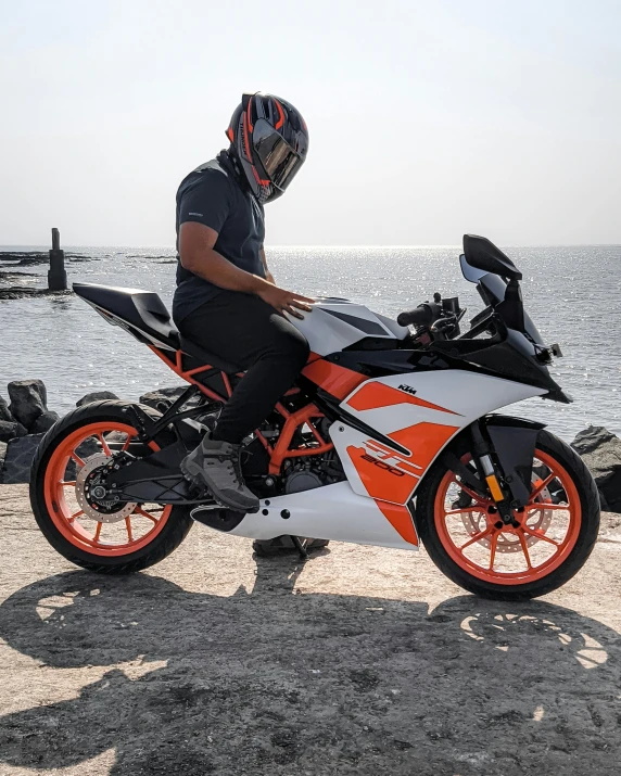 a man sitting on an orange motorcycle beside the water