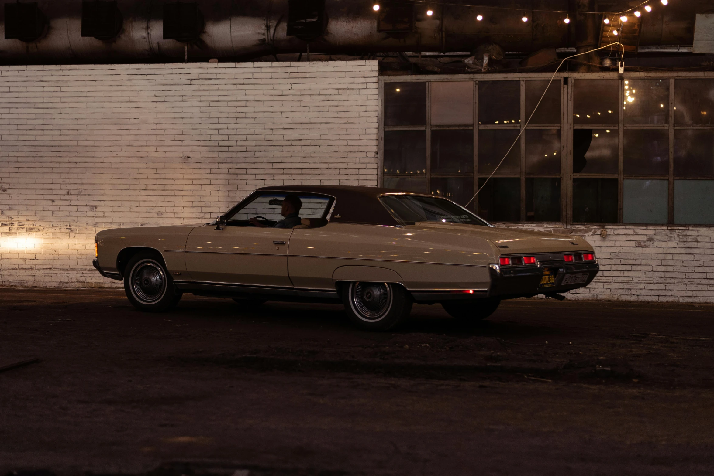 the tan car is parked in front of the white brick wall