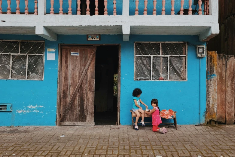 some s are sitting and playing near a blue building