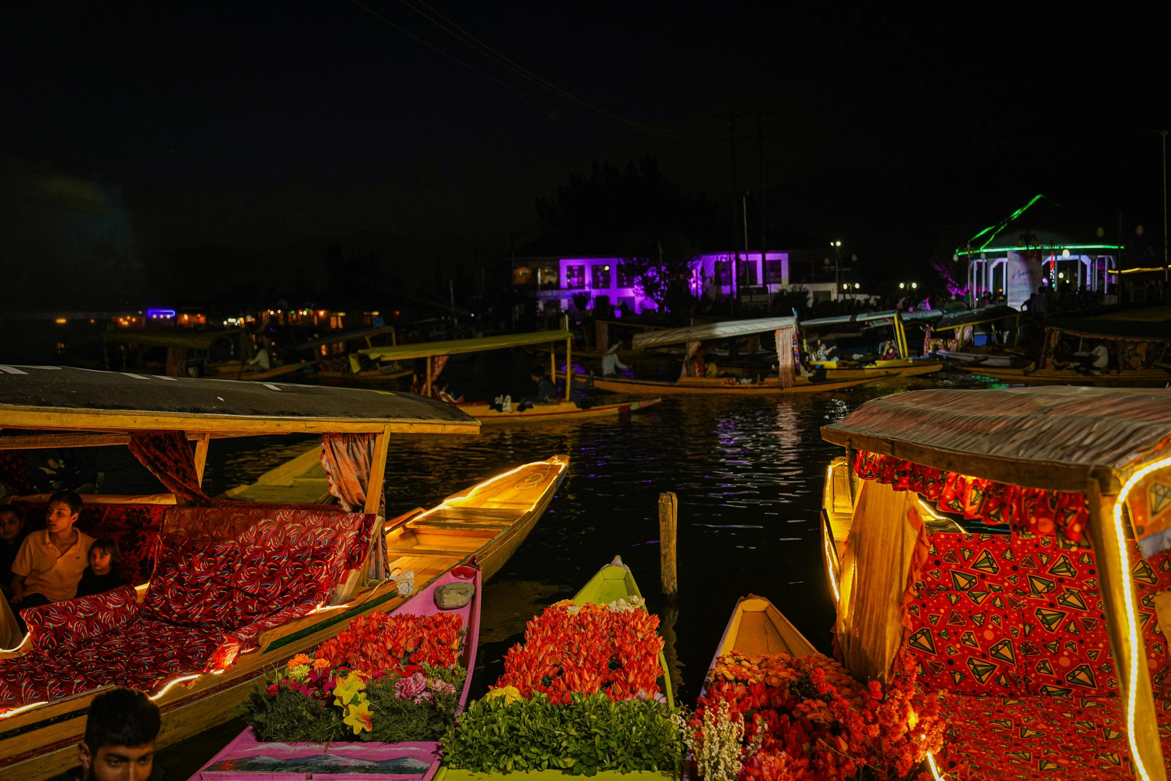 a boat is filled with colorful flowers by the shore