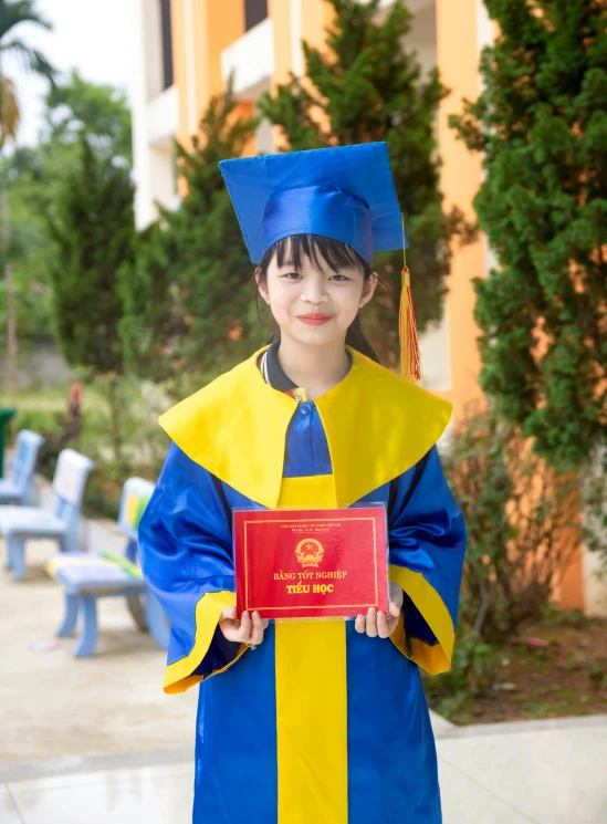 child holding red diploma in front of outdoor setting