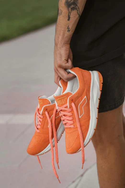 a man wearing orange running shoes while holding an orange pair