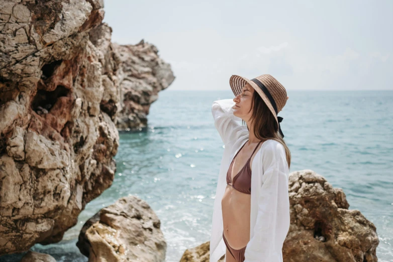 woman in a hat leaning on rocks by the ocean