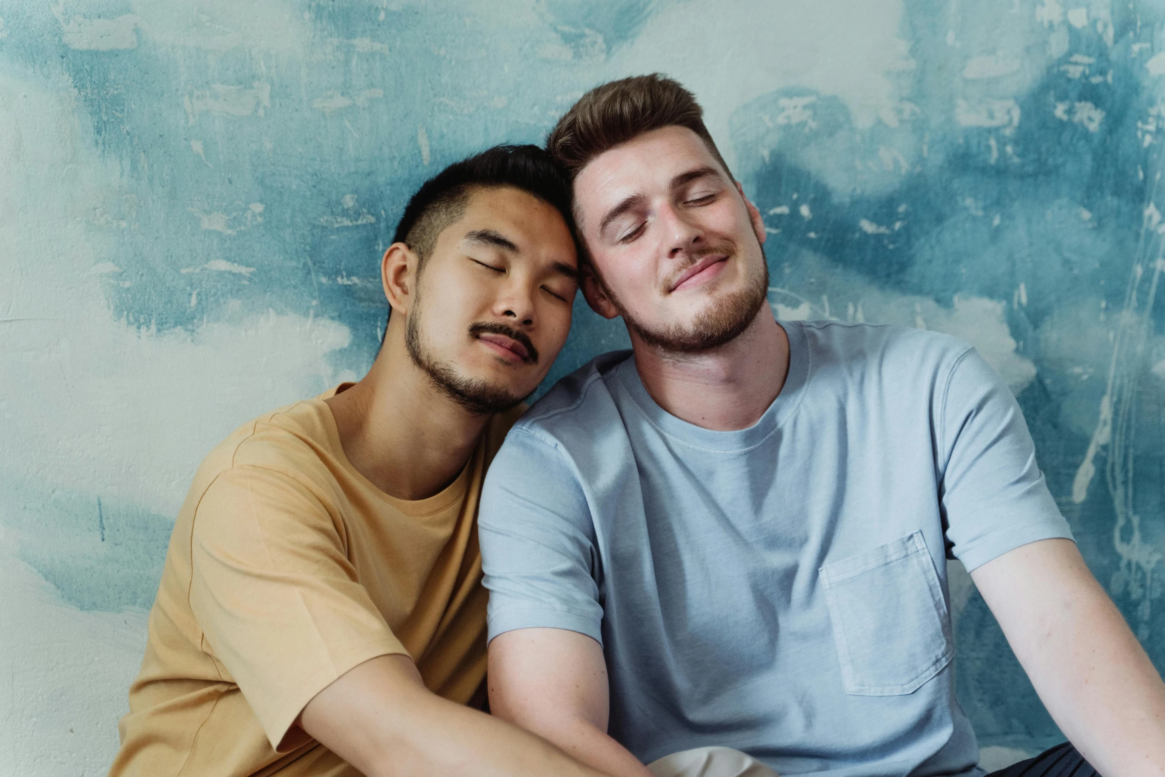 two males sitting together in front of a blue wall