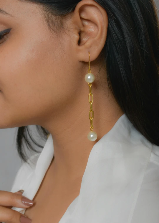 a woman with a long ear chain wearing a pair of white pearls