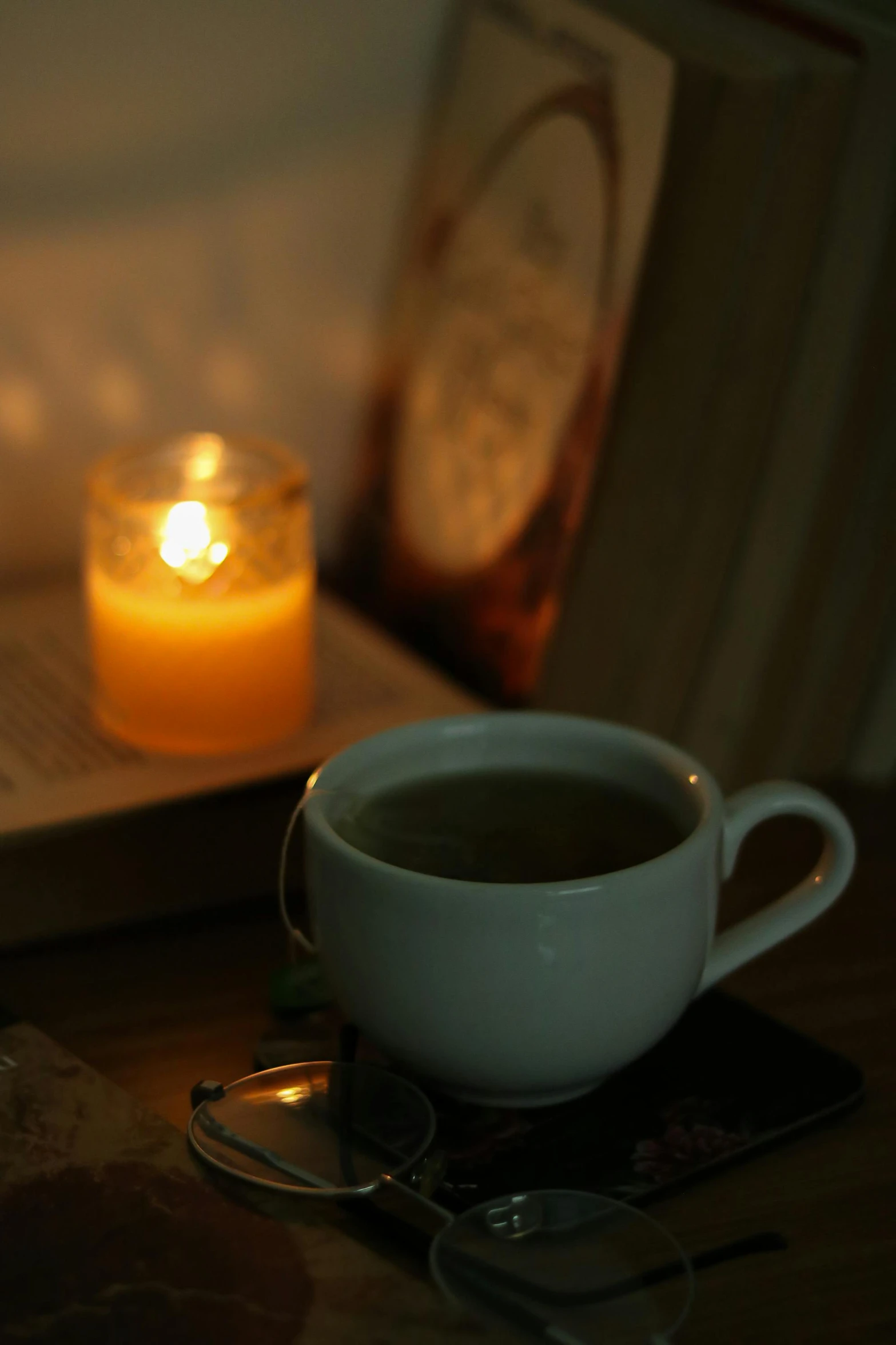 a candle sits next to a cup of coffee and a book