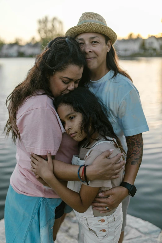 three friends hugging each other beside the water