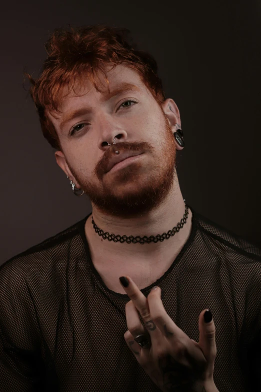 a man with red hair wearing a silver chain holding his hand out while making a cross gesture